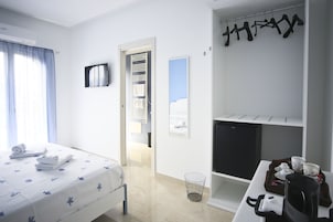 Habitación de hotel con una cama, una mesita con una bandeja de desayuno, un perchero y vistas al mar por la ventana.