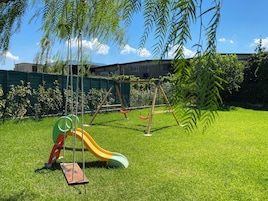 Un espacio al aire libre con césped, un tobogán y columpios.