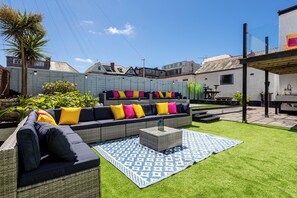 A backyard with a sectional sofa, a small table, and a patterned rug.