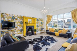 A living room with a fireplace, a television, a sofa set, and a large window with curtains.
