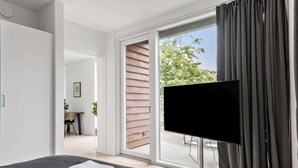 Ein modernes Hotelzimmer mit einem Bett, einem Flachbildfernseher und einer Schiebeglastür, die auf einen Balkon führt.