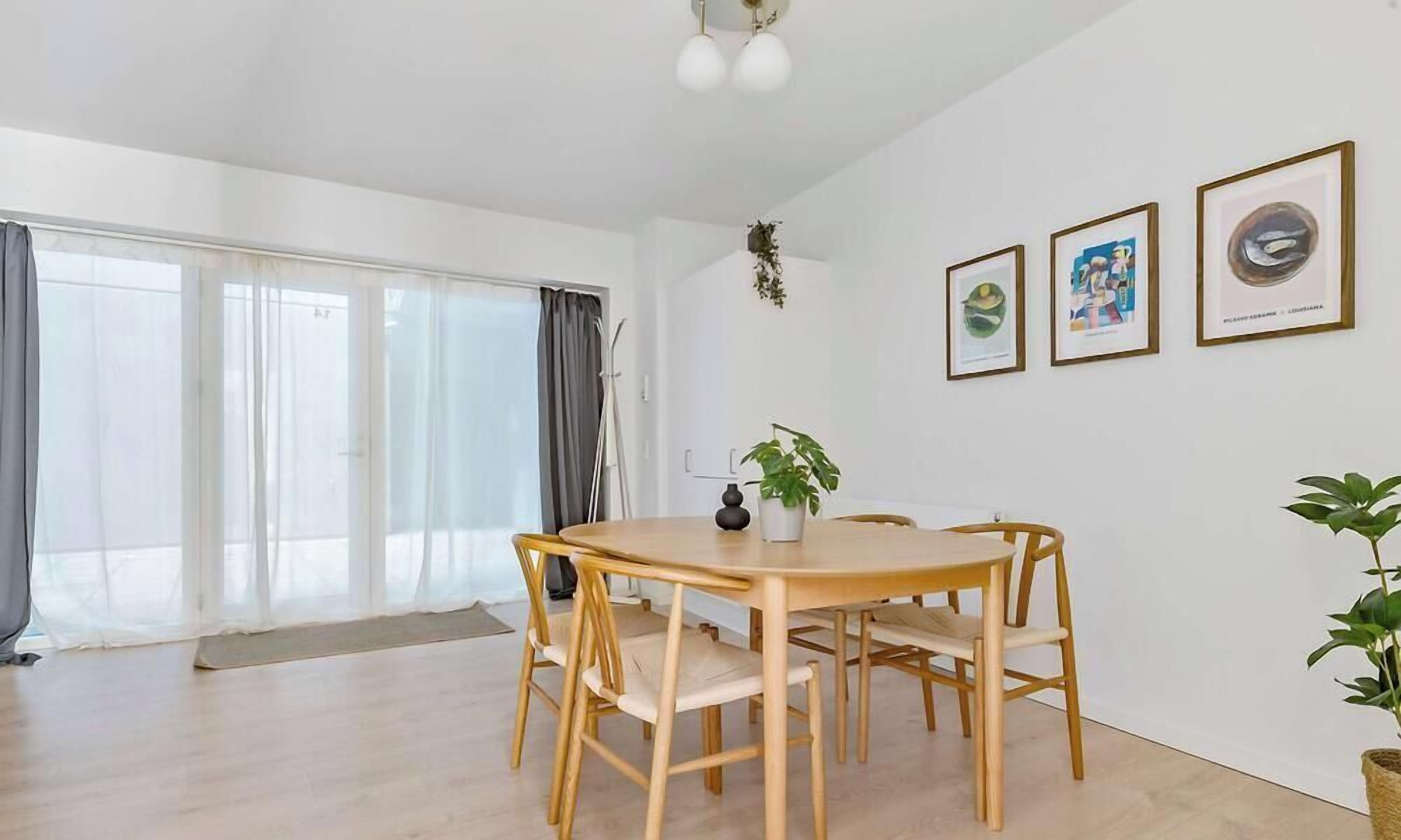 Una habitación amplia con una mesa de madera para comer, cuatro sillas, una planta en maceta y cuadros en la pared.