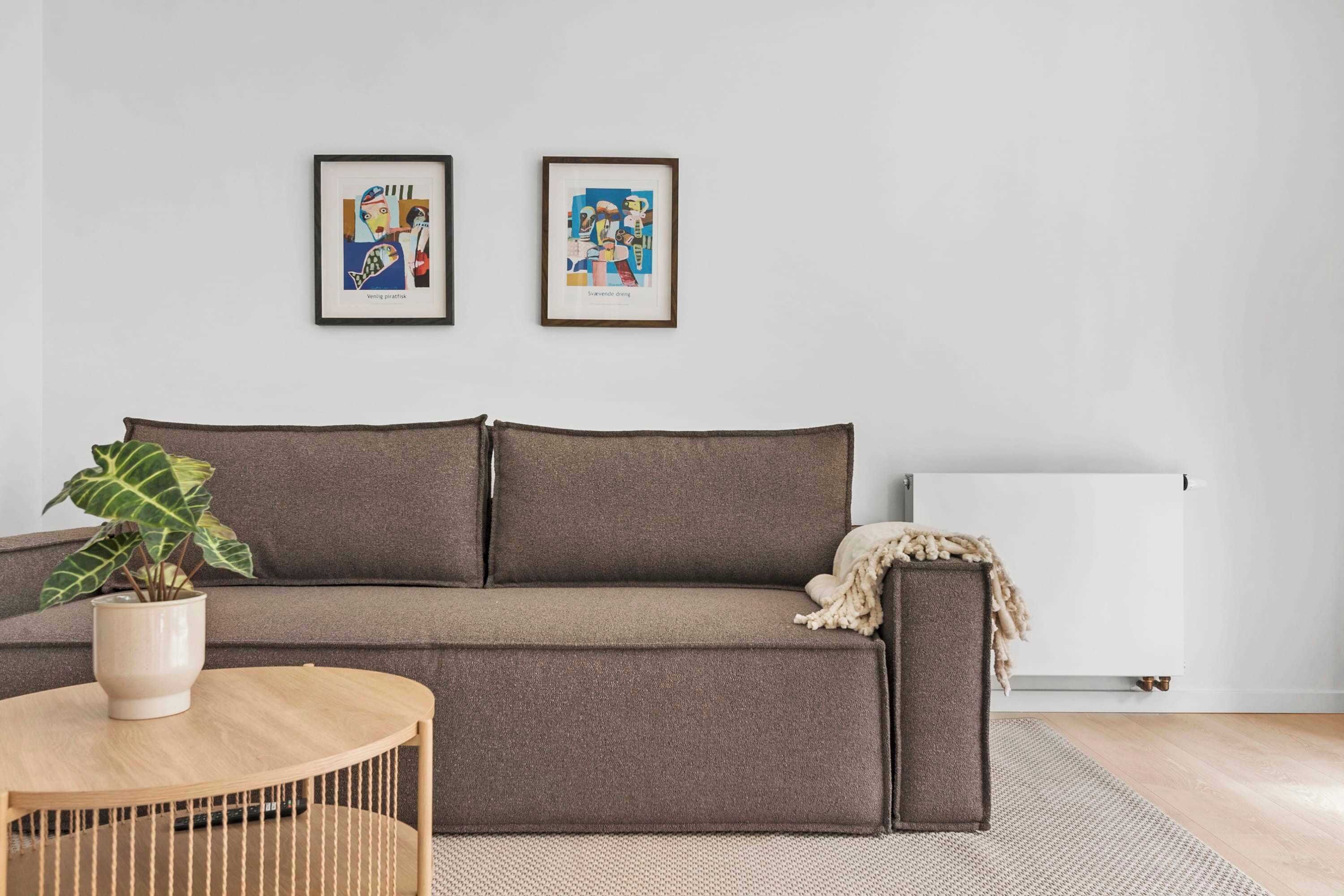 Ein stilvolles Wohnzimmer in neutralen Farben mit einem braunen Sofa, einem runden Couchtisch und zwei gerahmten Kunstwerken an der Wand.