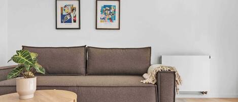 Ein stilvolles Wohnzimmer in neutralen Farben mit einem braunen Sofa, einem runden Couchtisch und zwei gerahmten Kunstwerken an der Wand.