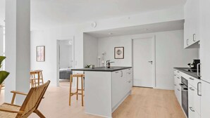 Une cuisine moderne avec des meubles blancs, un îlot central et un coin repas doté de chaises en bois.