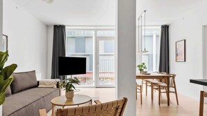 Un salon moderne comprenant un canapé, un téléviseur, une table à manger avec des chaises et un balcon avec des rideaux.