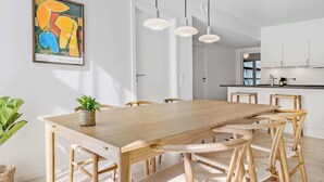 Un espace repas avec une table et des chaises en bois, un tableau abstrait suspendu au mur et des luminaires suspendus.