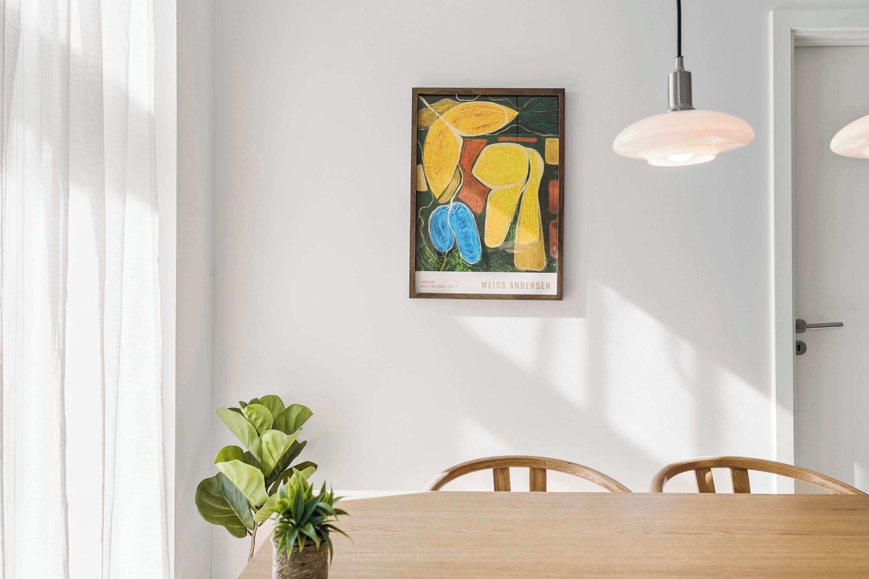 Ein Essbereich mit Holztisch, Stühlen, einem Blumentopf und einem gerahmten, abstrakten Gemälde an der Wand.