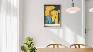 Ein Essbereich mit Holztisch, Stühlen, einem Blumentopf und einem gerahmten, abstrakten Gemälde an der Wand.
