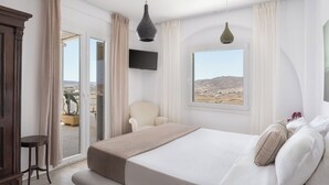 A hotel room with a large bed, a chair, a TV, and a window with a desert view.