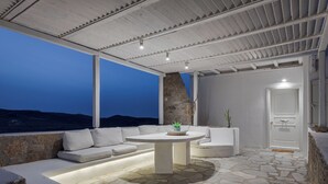An outdoor seating area with stone flooring, white furniture, and a view of the landscape.