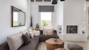 A modern living room with a sectional sofa, a round wooden coffee table, a fireplace, and a large window with a view.