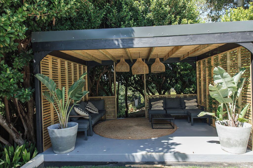 An outdoor patio with a wooden pergola, seating area, and potted plants.