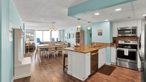 Une cuisine moderne dotée d’un îlot central, d’appareils électroménagers en acier inoxydable et d’un coin repas avec une grande table et des chaises.