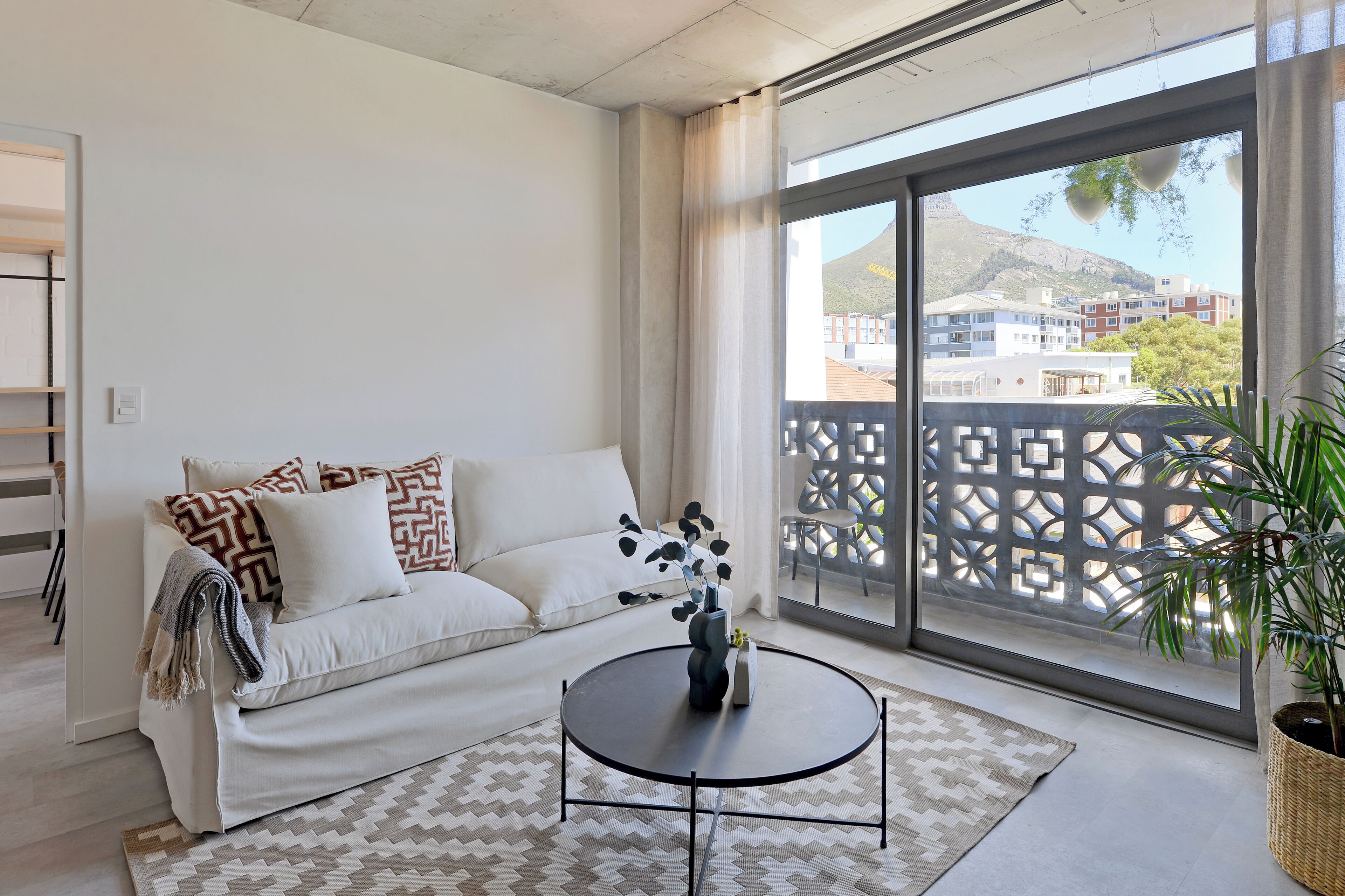 A modern living room with a sofa, a coffee table, and a large window with a view of buildings and a mountain.