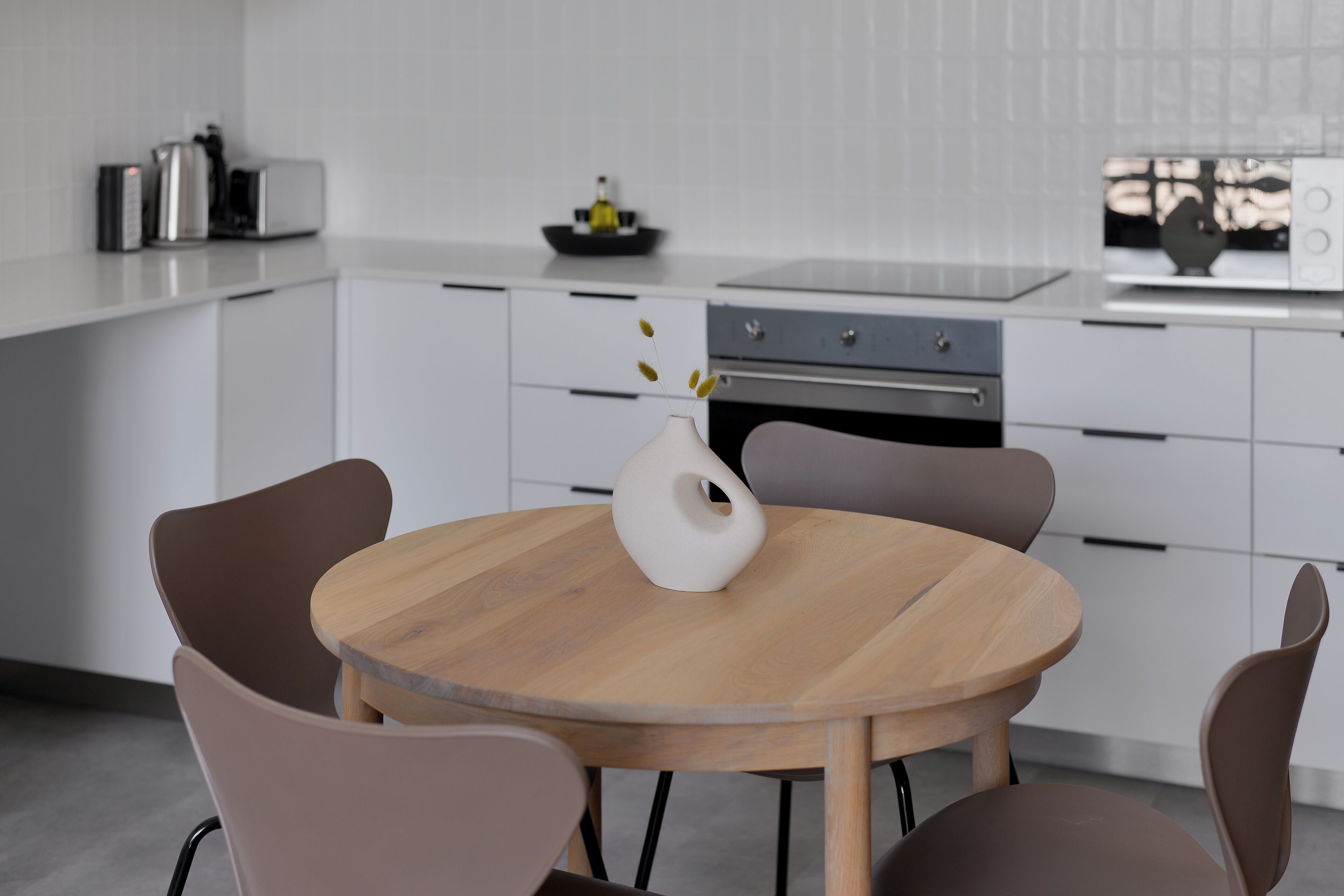Een moderne keuken met witte kastjes, een houten eettafel en een vaas met bloemen.