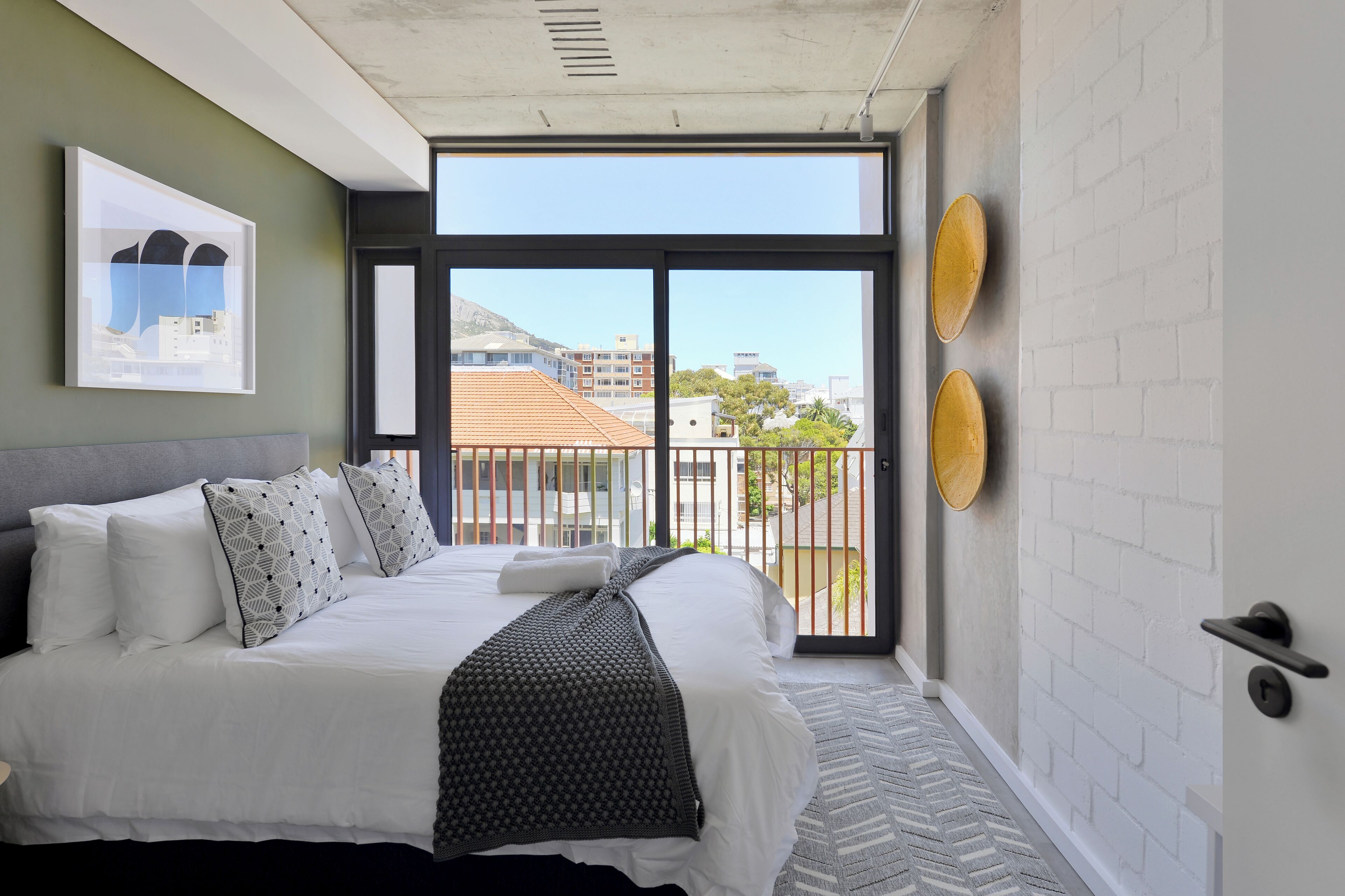 A modern hotel room with a large bed, a view of the city through a sliding door, and a balcony with decorative plates.