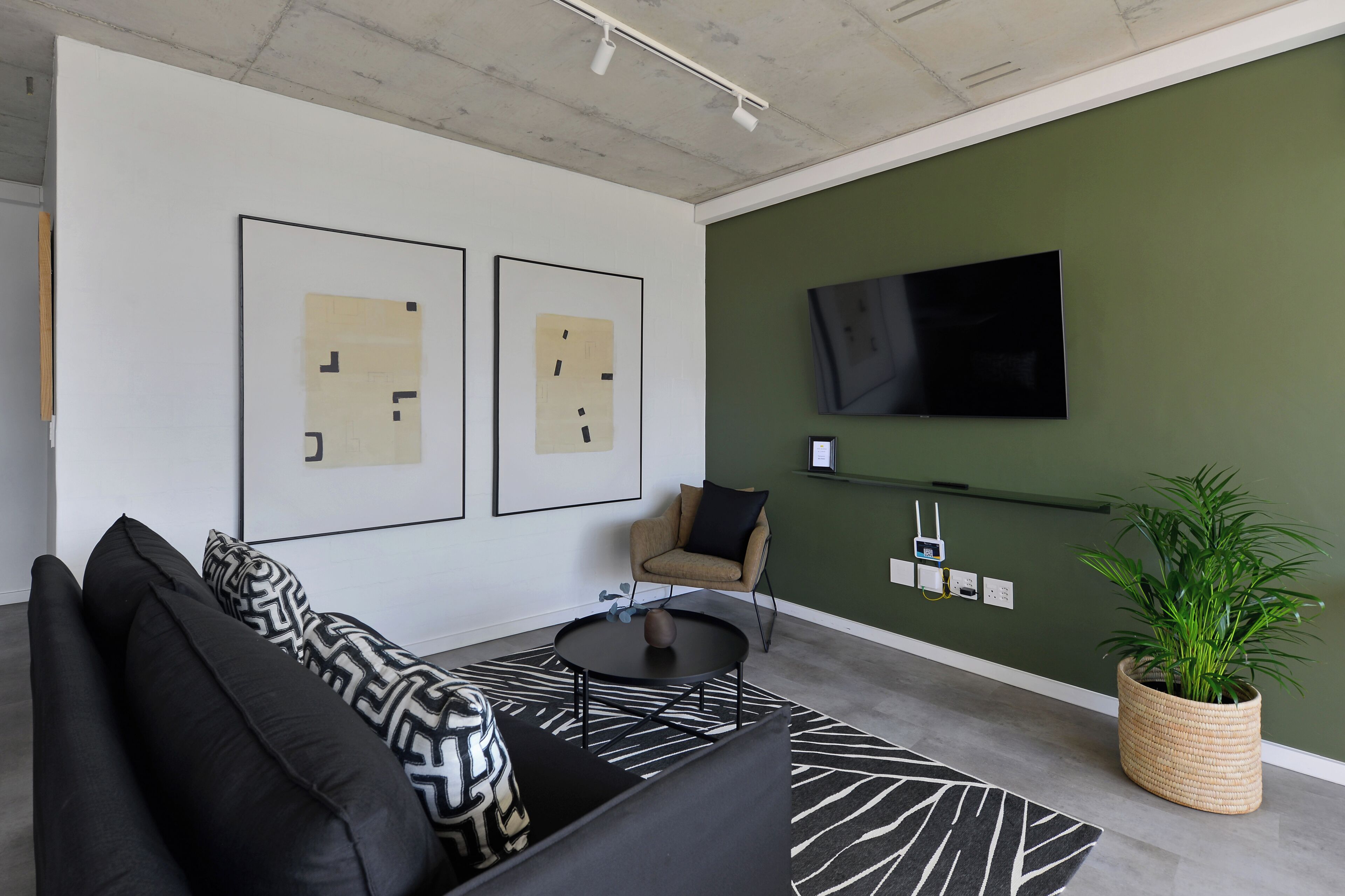 A modern living room with a black and white patterned sofa, a round coffee table, a green accent wall, a mounted TV, and a potted plant.