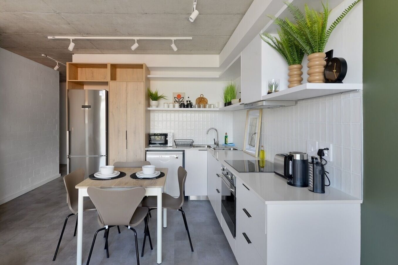 A modern kitchen with white cabinetry, a dining table with chairs, a refrigerator, a microwave, and a sink.