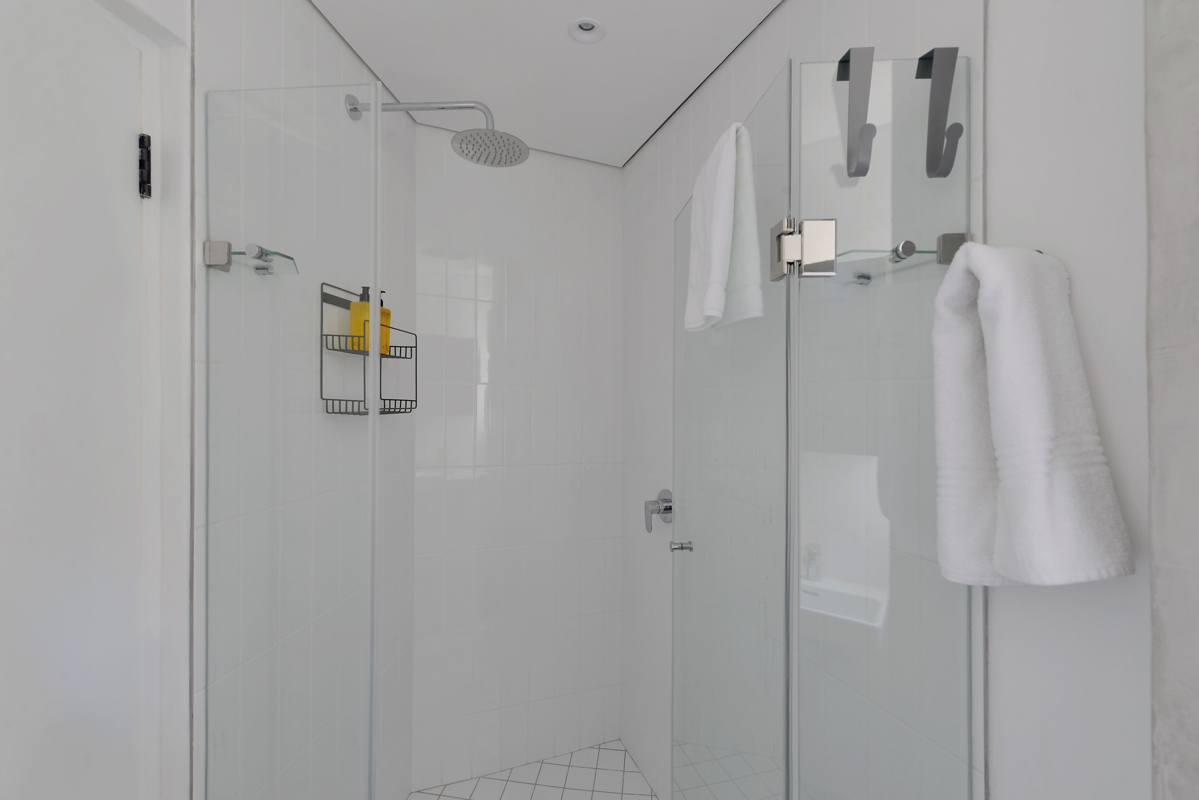 Une salle de bain moderne avec une douche à l’italienne en verre, des carreaux blancs et un porte-serviettes.