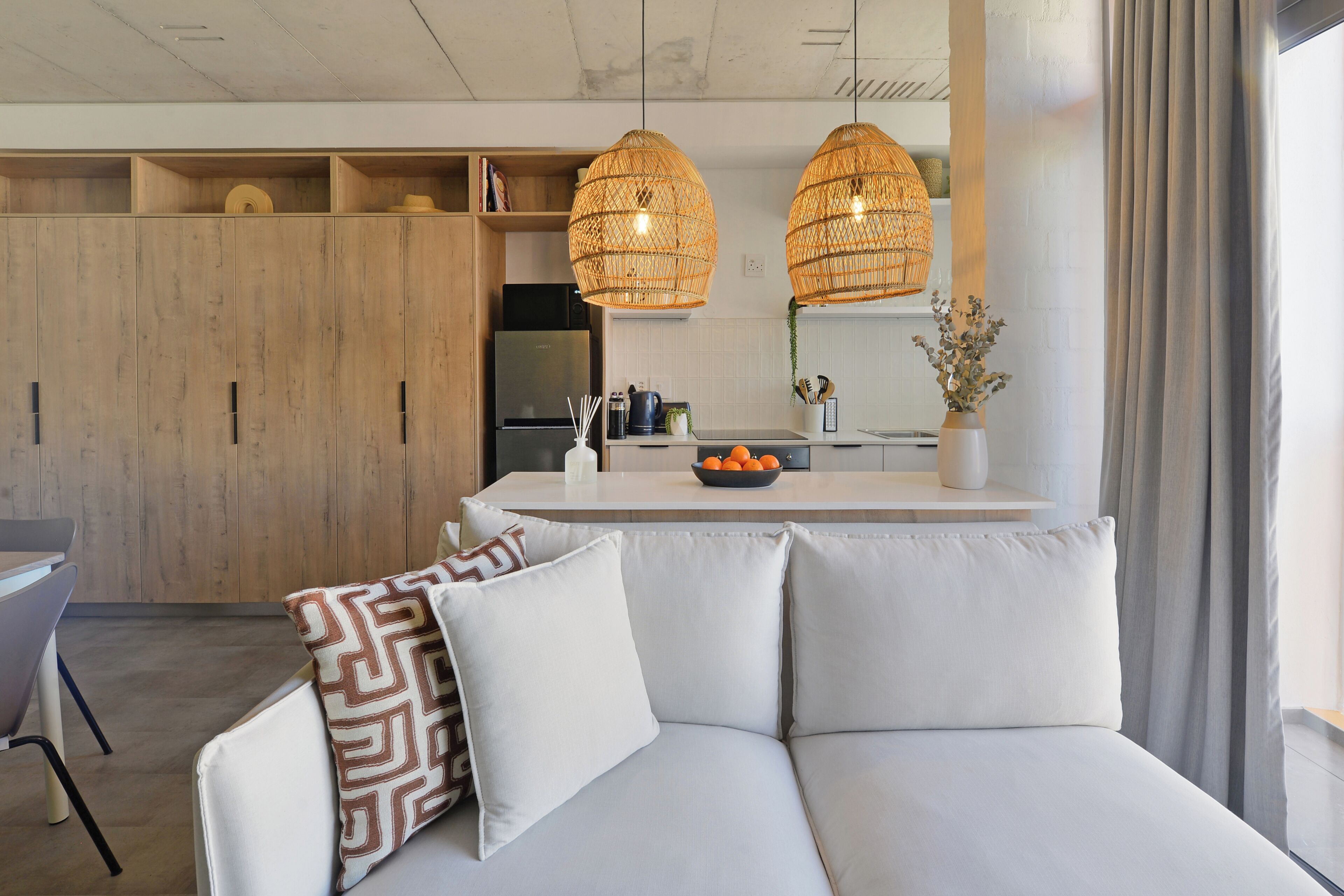 A modern kitchen with wooden cabinets, a built-in fridge, and a central island with a bowl of fruit.