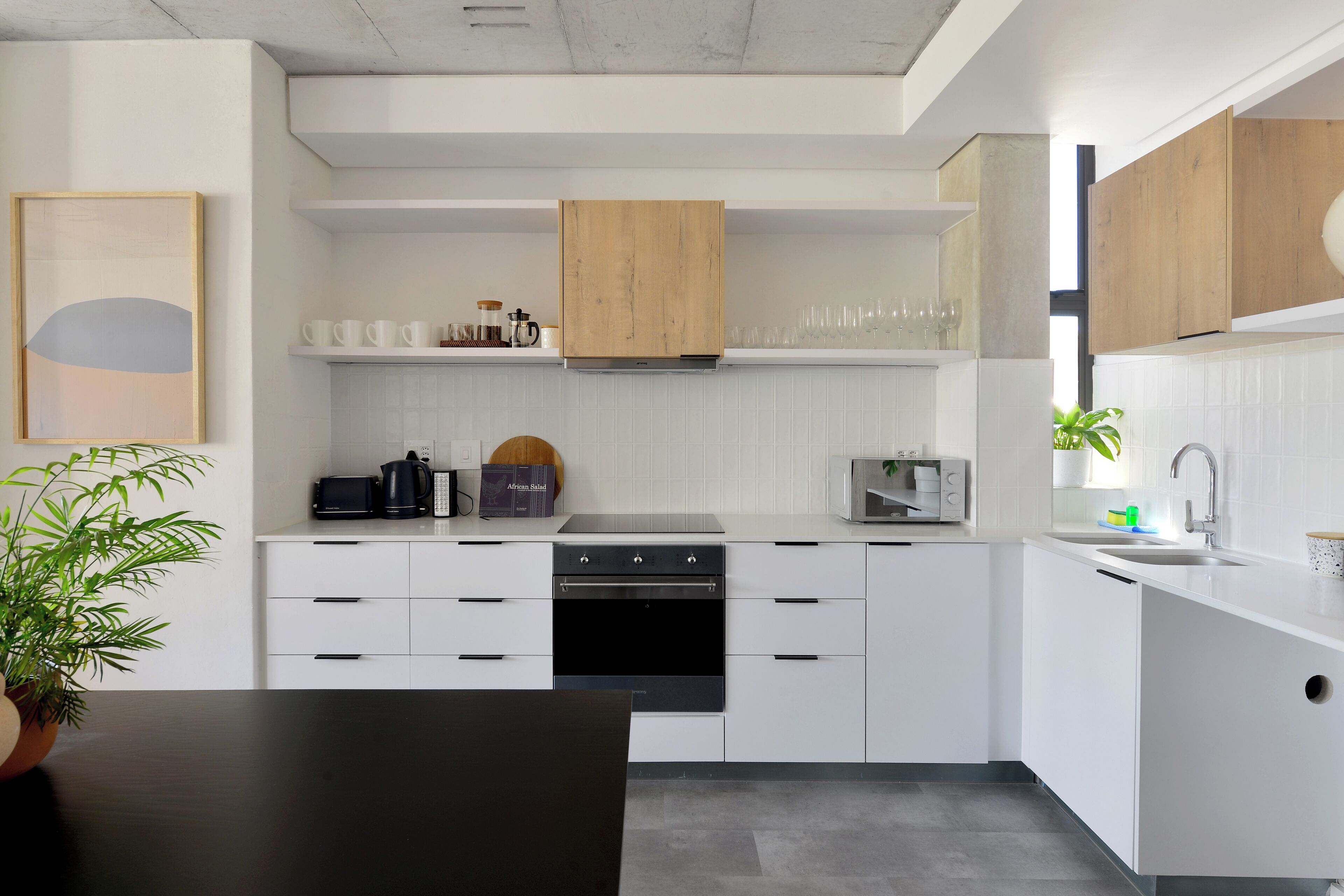 A modern kitchen with white cabinetry, a black oven, and a wooden cabinet above the stove.