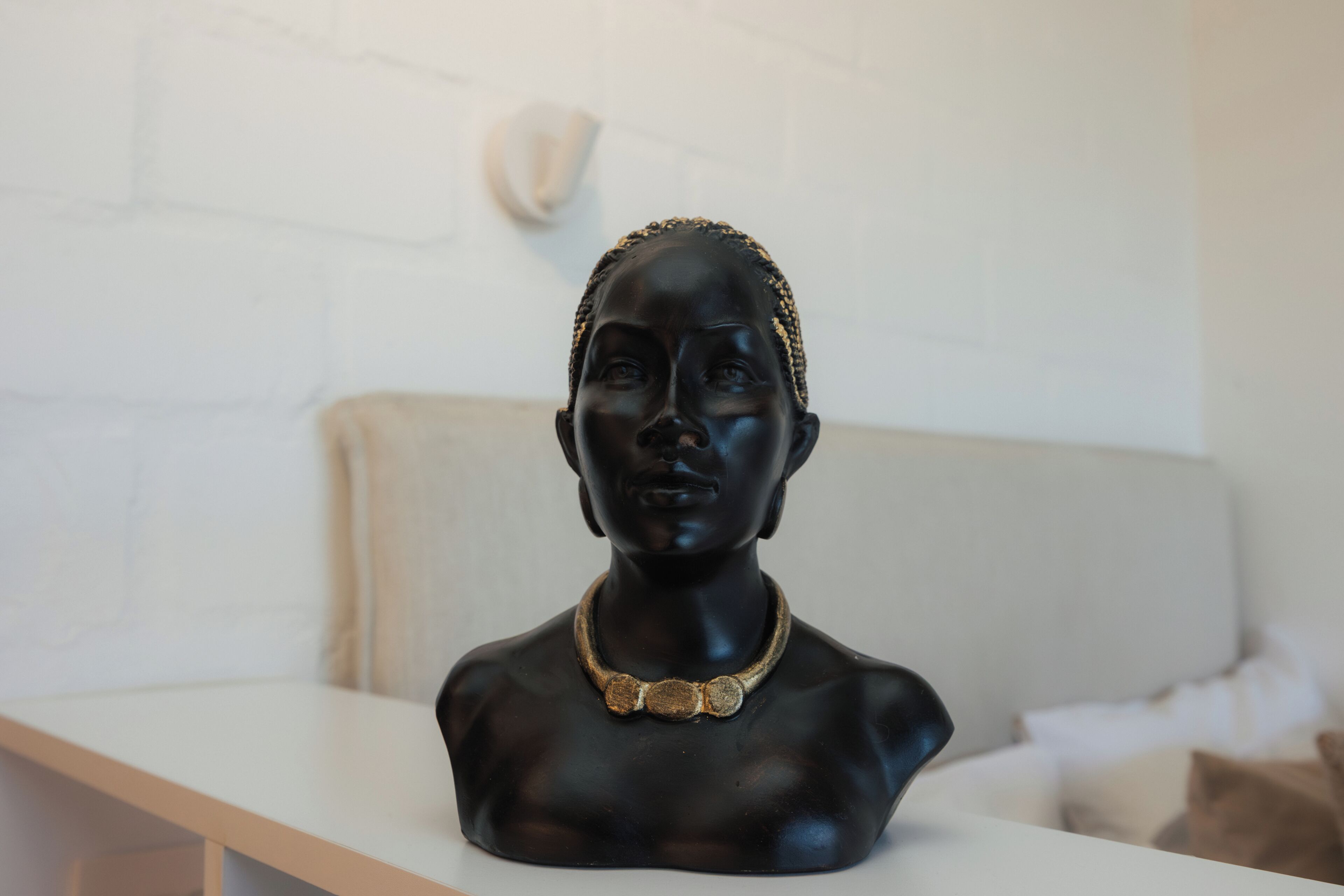 Escultura tipo busto sobre una mesa blanca frente a una pared blanca.