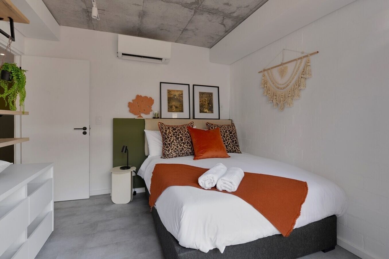 A modern bedroom with a bed, a bedside table, a lamp, and a wall-mounted air conditioner.