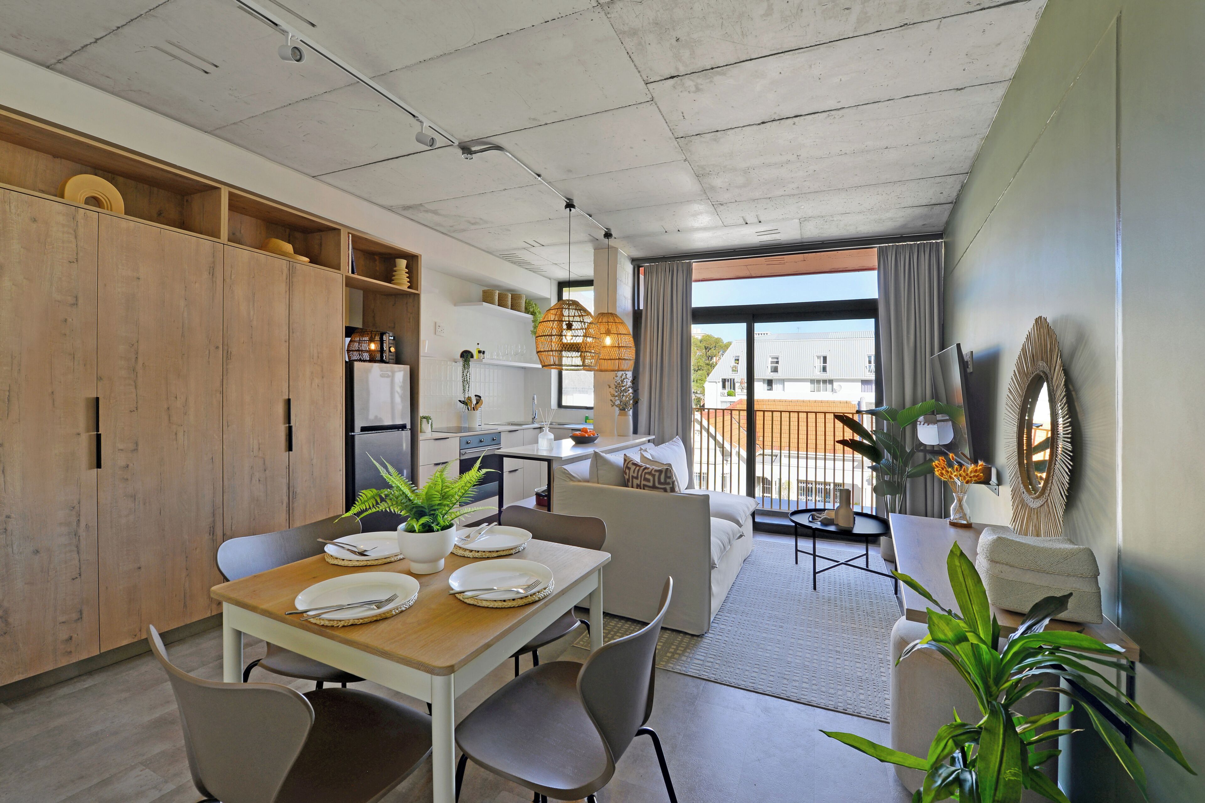 A modern kitchen with a dining area, wooden cabinets, and a view to the outside.