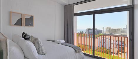 A modern bedroom with a large bed, two framed artworks, and a balcony with a red railing.