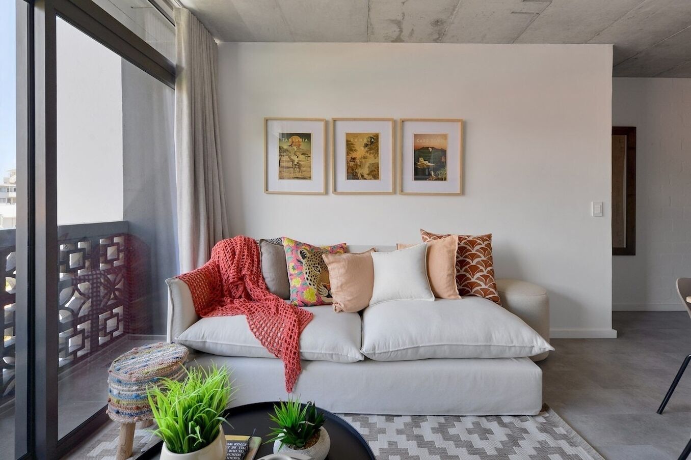 Ein modernes Wohnzimmer mit einer Couch, Kissen, einer roten Decke und gerahmten Bildern an der Wand.