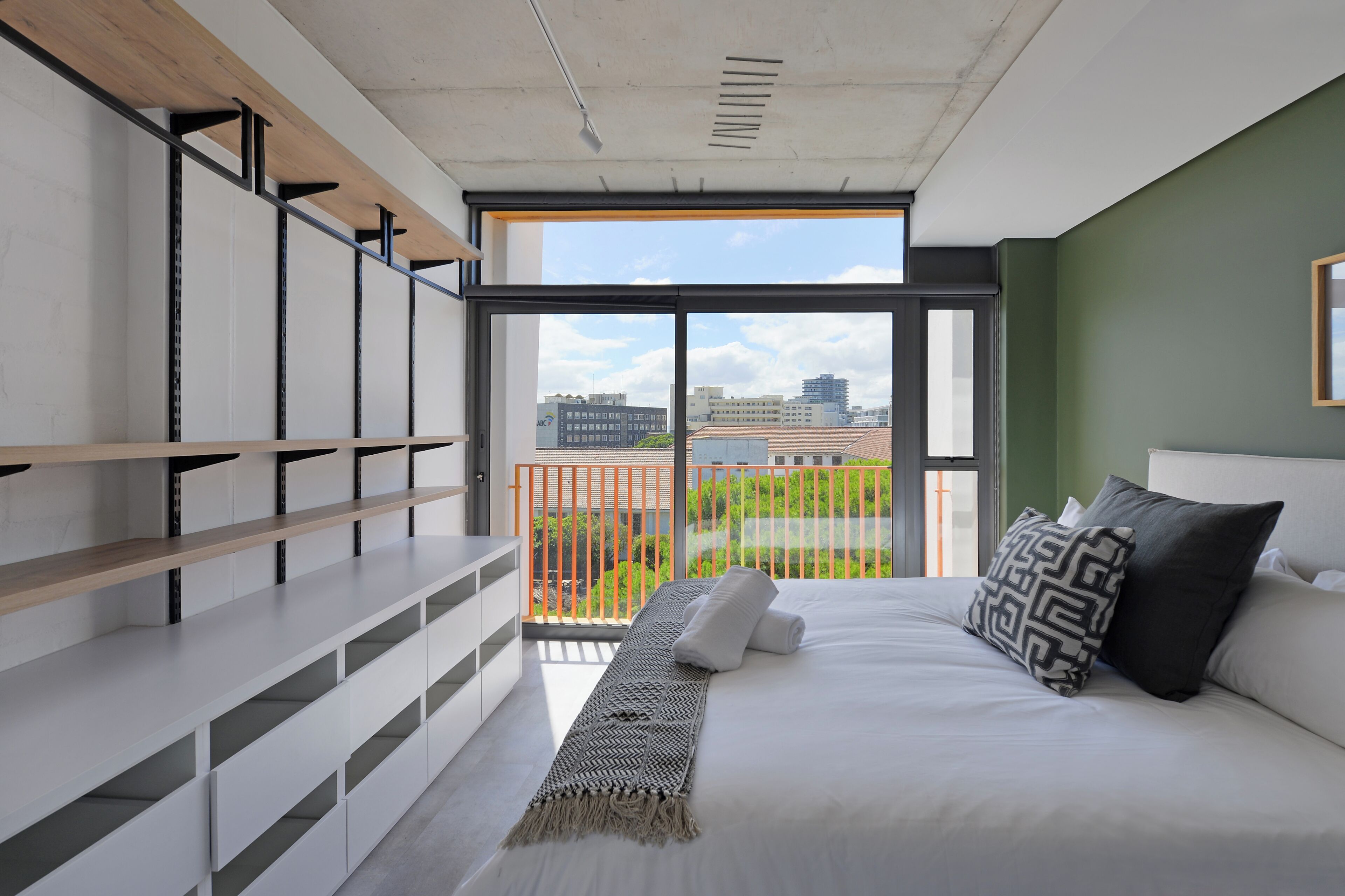 A modern bedroom with a large window, a bed with pillows, a bedside table, and built-in shelving.
