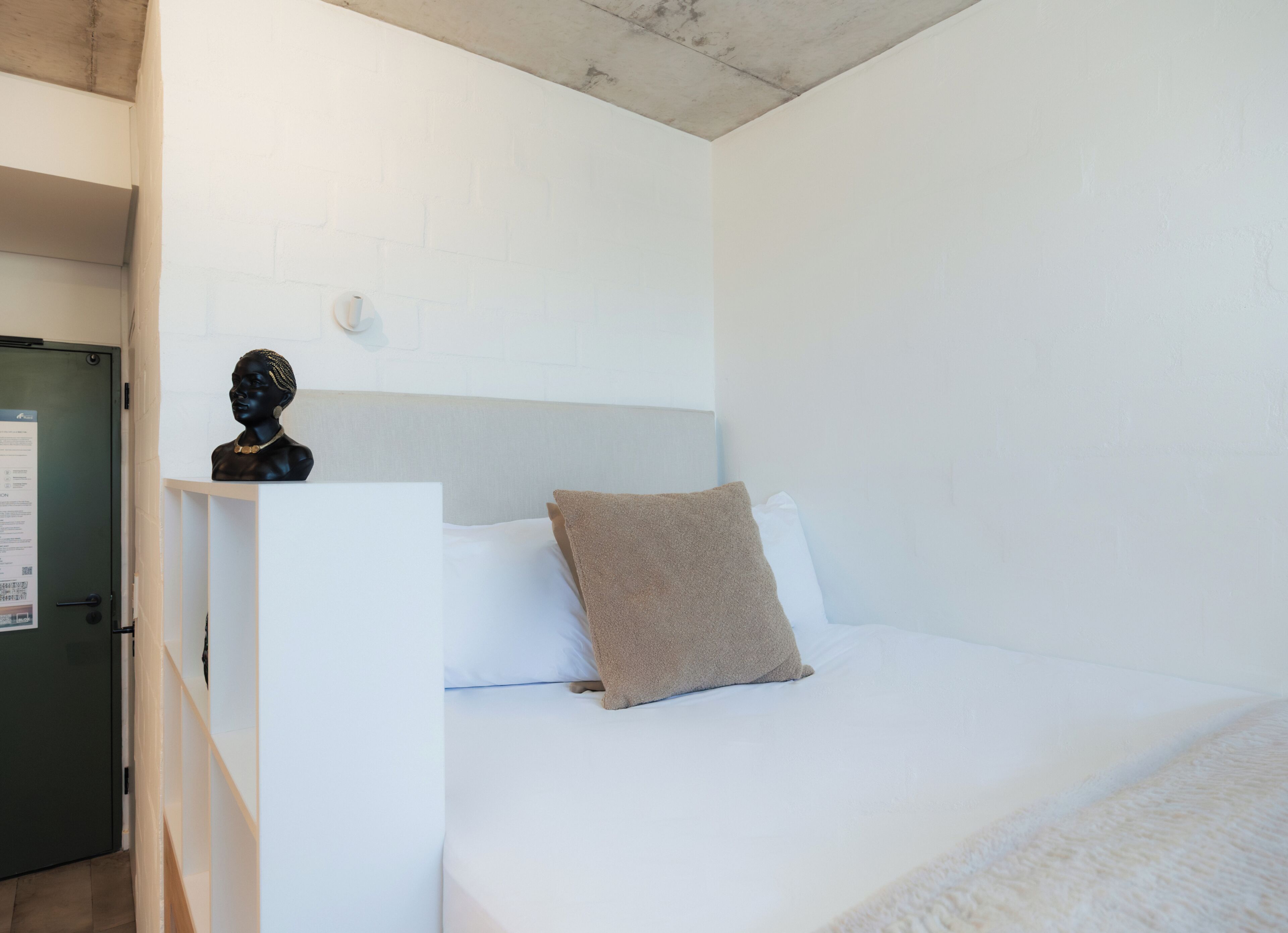 A bedroom with a bed, a pillow, a nightstand, and a bust sculpture.