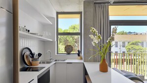 Une cuisine moderne avec des meubles blancs, un four encastré et une fenêtre donnant sur un paysage verdoyant et des bâtiments.