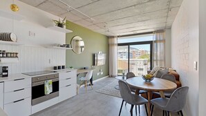 A modern kitchen with white cabinets, a built-in oven, and a dining area with a round table and grey chairs.