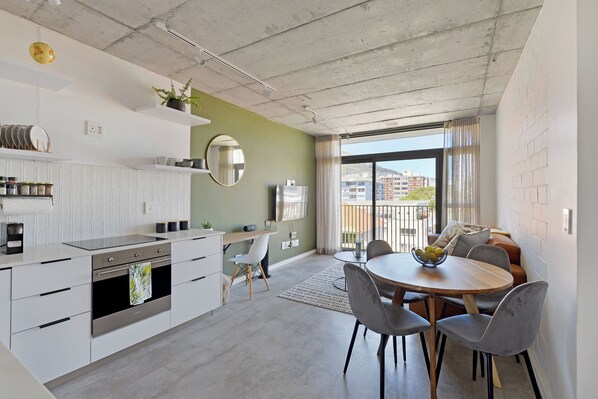 A modern kitchen with white cabinets, a built-in oven, and a dining area with a round table and grey chairs. - SIX ON N - Fluent Serviced Apartments (Cape Town)
