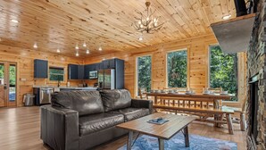 A cabin interior with a wooden ceiling, a leather sofa, a dining table, and a kitchen area with a refrigerator and cabinets. - New Listing! Indoor pool, hot tub, theater, bocce, billiards, & firepit. (Sevierville)