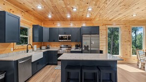 A modern kitchen with wooden walls, stainless steel appliances, and a central island with bar stools. - New Listing! Indoor pool, hot tub, theater, bocce, billiards, & firepit. (Sevierville)