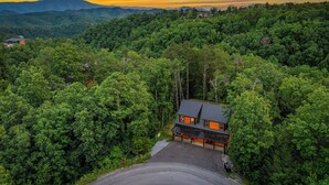 A house surrounded by dense forest with a clear driveway and a mountain range in the background. - New Listing! Indoor pool, hot tub, theater, bocce, billiards, & firepit. (Sevierville)