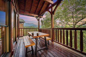 A wooden deck with a picnic table and benches, overlooking a mountainous landscape.