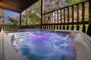 A hot tub with a wooden deck and railing, surrounded by trees.