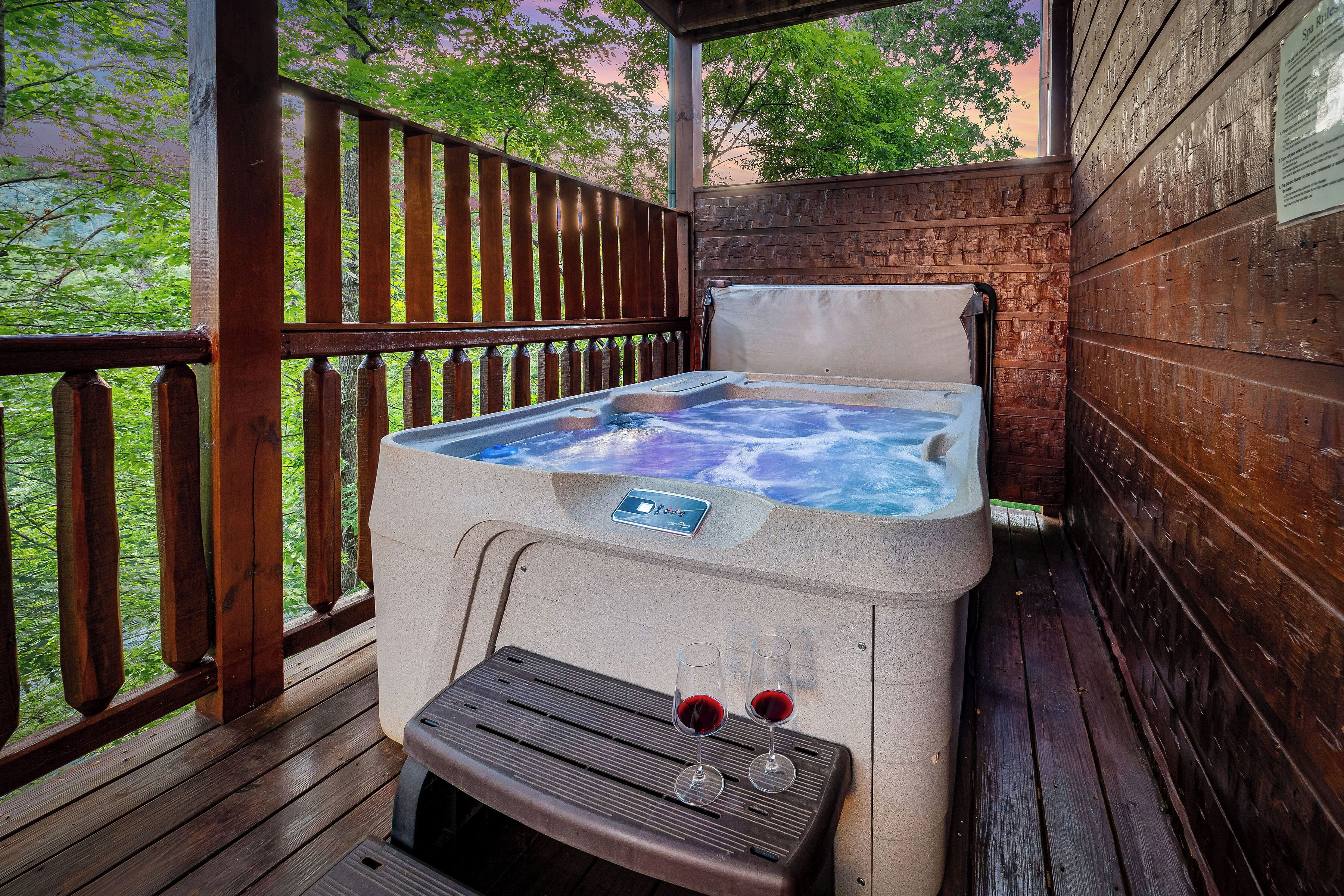 A hot tub with two glasses of red wine on a wooden deck.
