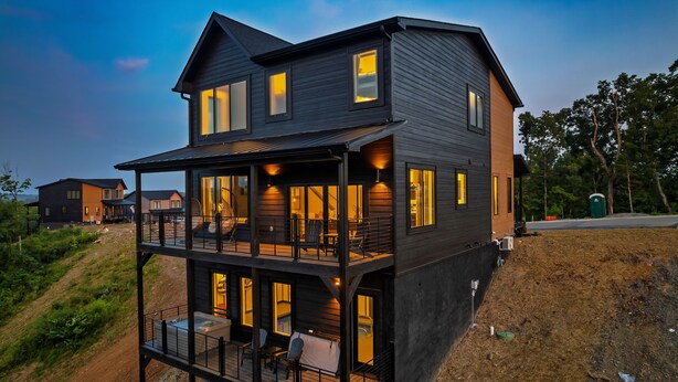 A two-story modern house with a balcony, large windows, and a well-lit interior. - Brand New Modern Luxe 6 Bed w/ Arcade Games, Indoor Pool, Great Views! (Sevierville)