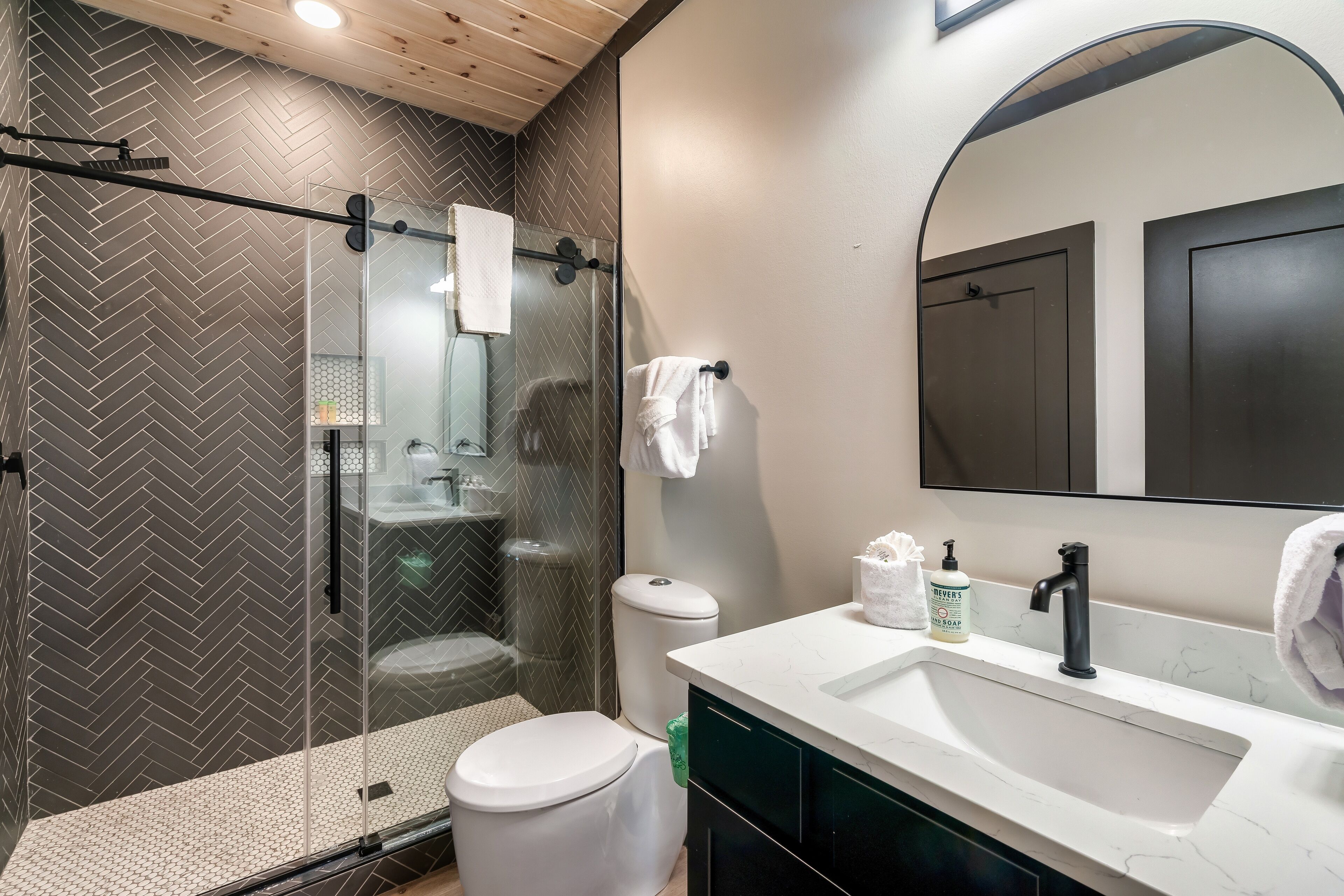 A modern bathroom with a glass-enclosed shower, a white toilet, a sink with a marble countertop, and a large mirror above the sink.