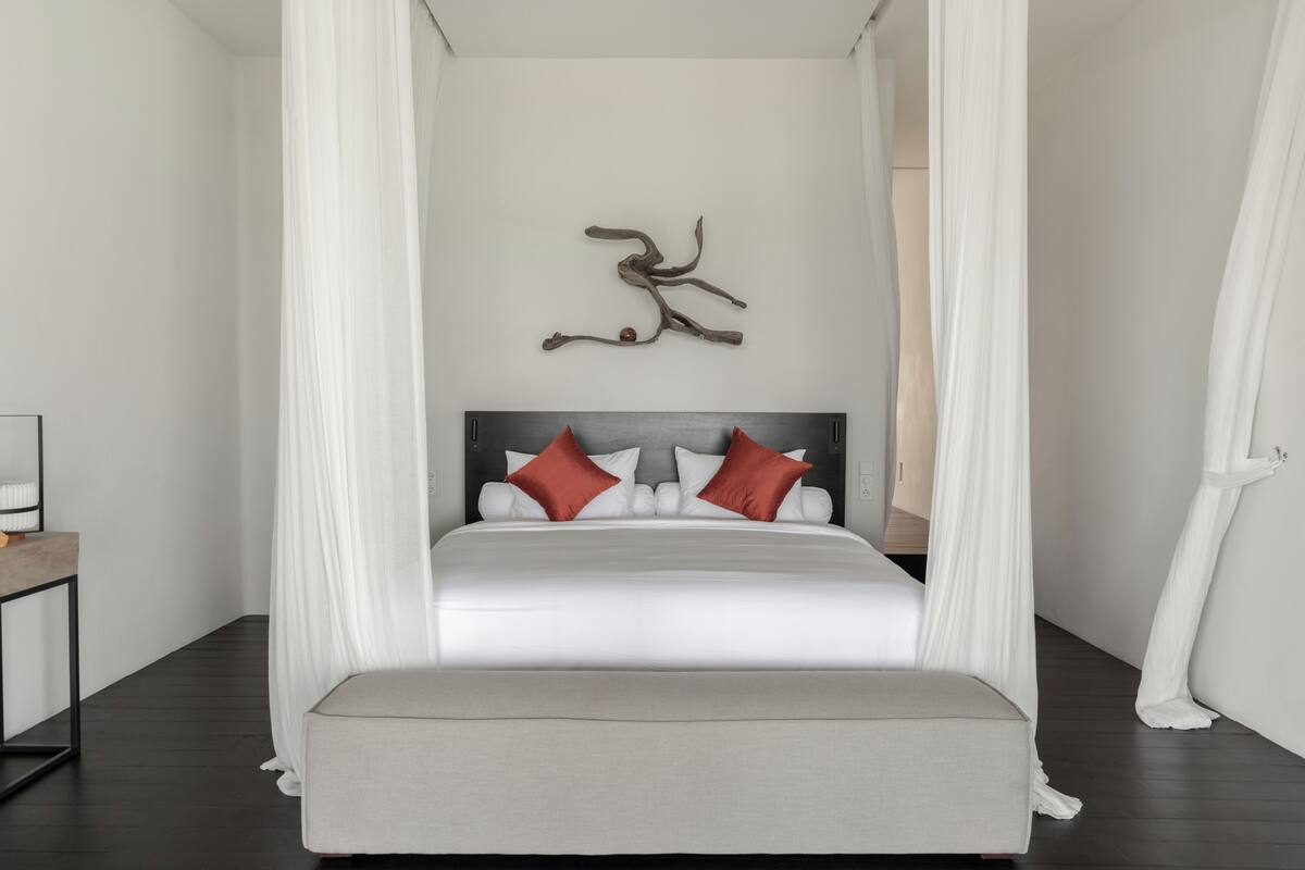 A modern bedroom with a canopy bed, a decorative wall piece, and a minimalist nightstand.