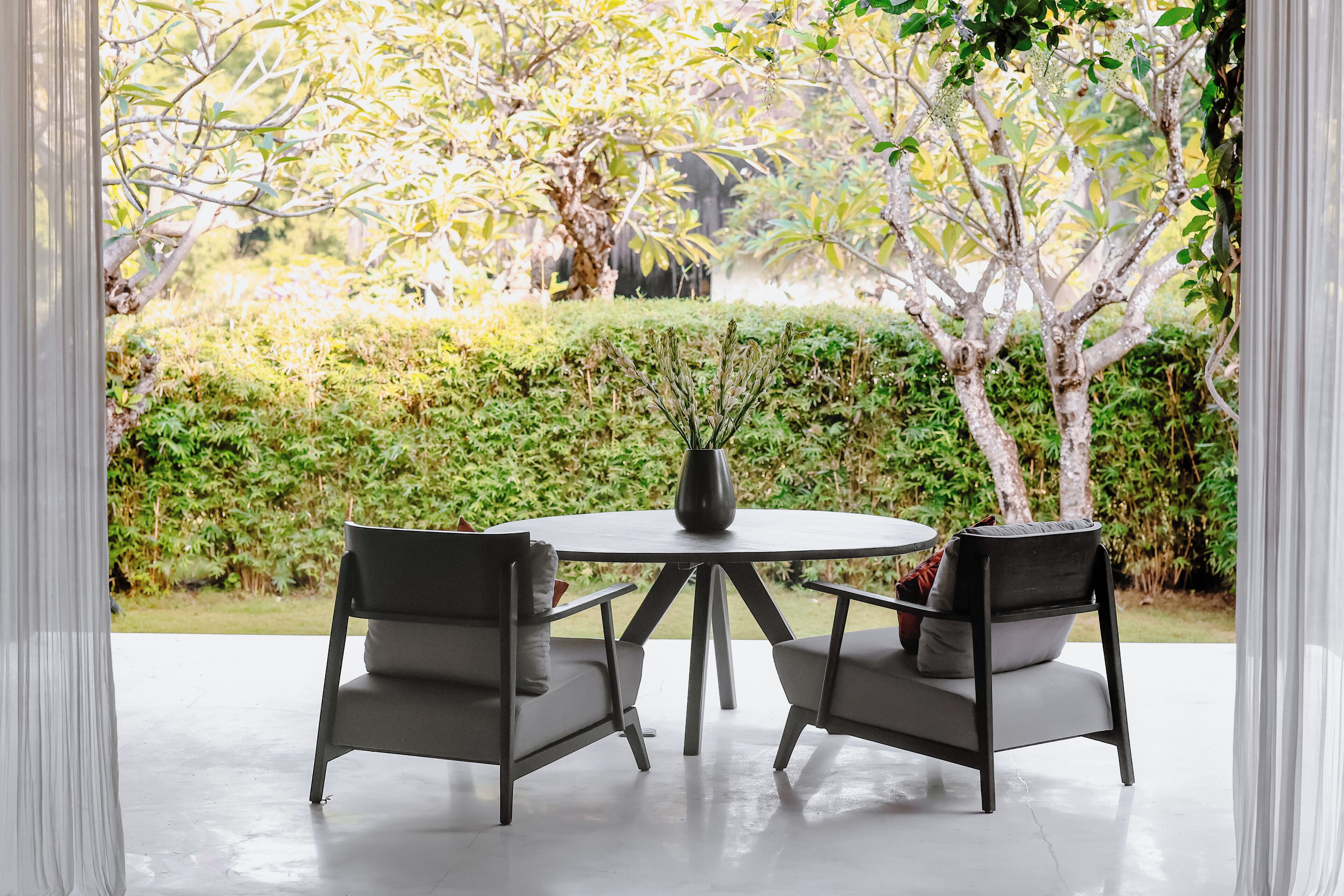 A patio with two chairs and a table, surrounded by greenery and trees.