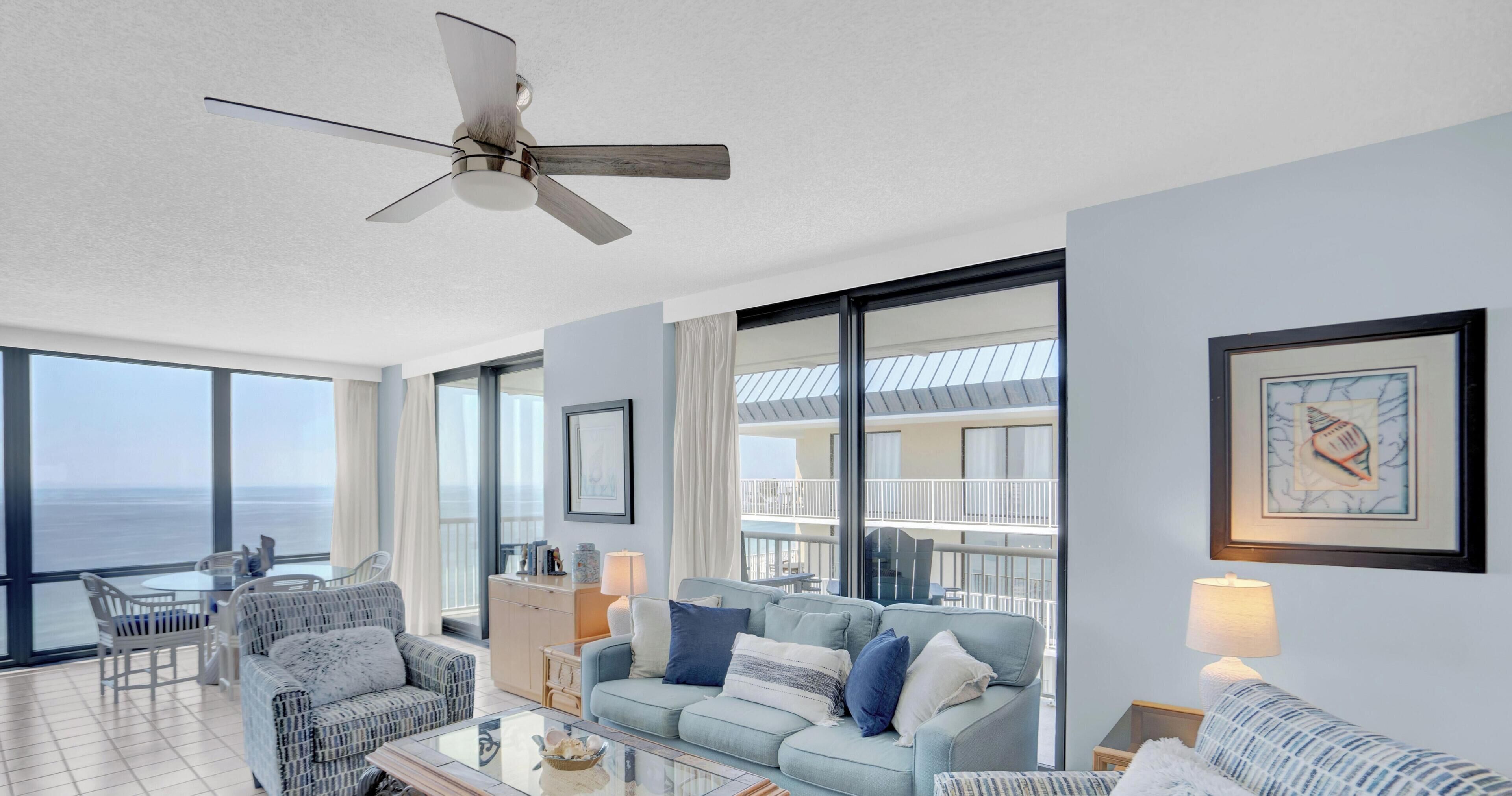 Un salon spacieux avec un balcon, de grandes fenêtres et un ventilateur de plafond.