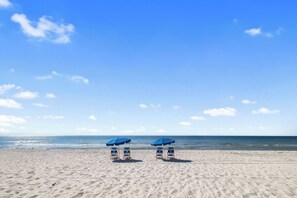 A beach with two blue umbrellas and beach chairs.