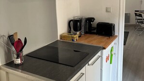 A compact kitchen with a black induction cooktop, white cabinets, and a wooden countertop. - Cozy Avignon Apartment Intra muros  (Avignon)