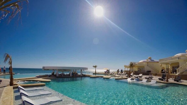 A pool with clear water, sun, and a view of the ocean.
